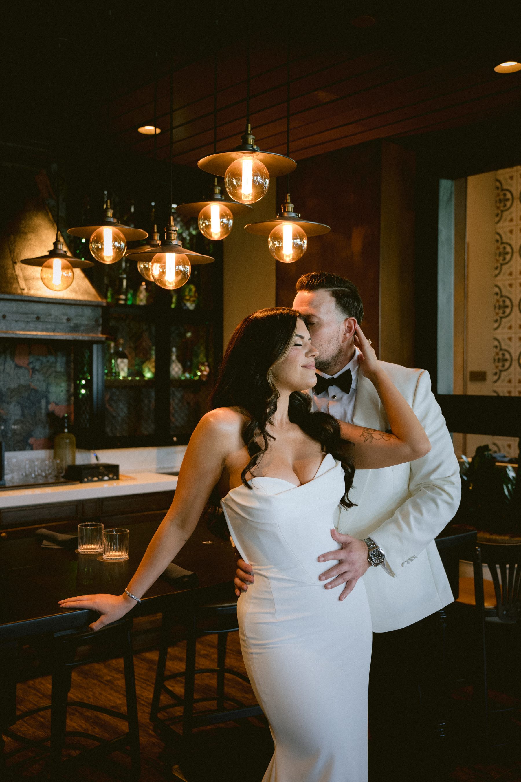 Bride and groom sharing a close moment under warm pendant lights at a bar
