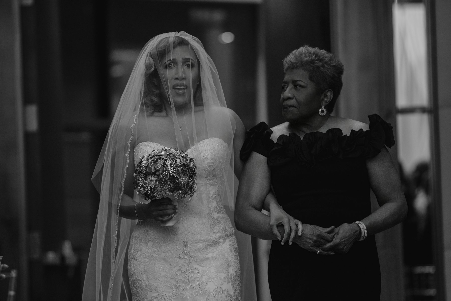 Black and white photo of a bride and her mother walking arm in arm