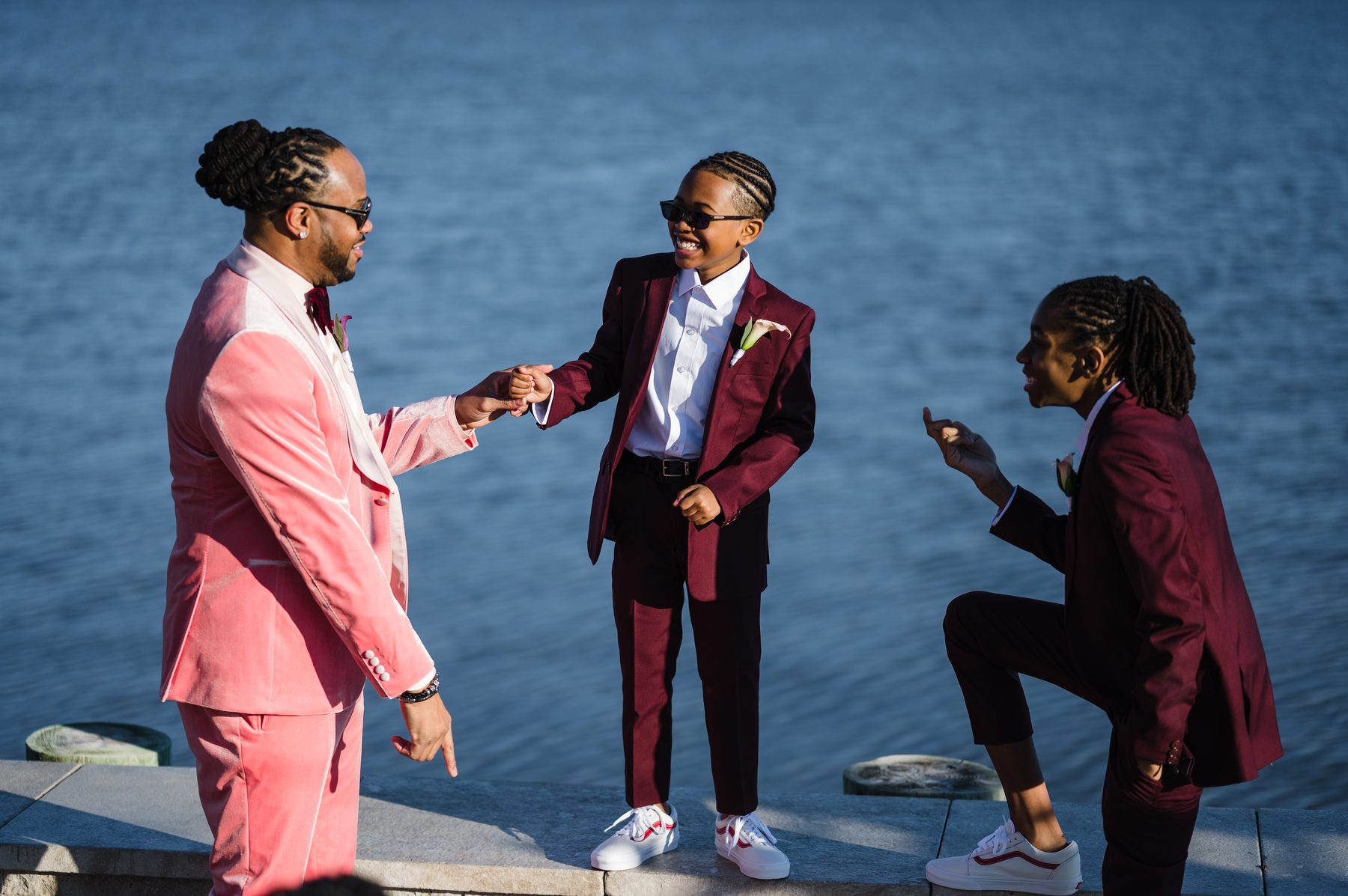 Groom fist-bumping his sons in colorful suits beside the water