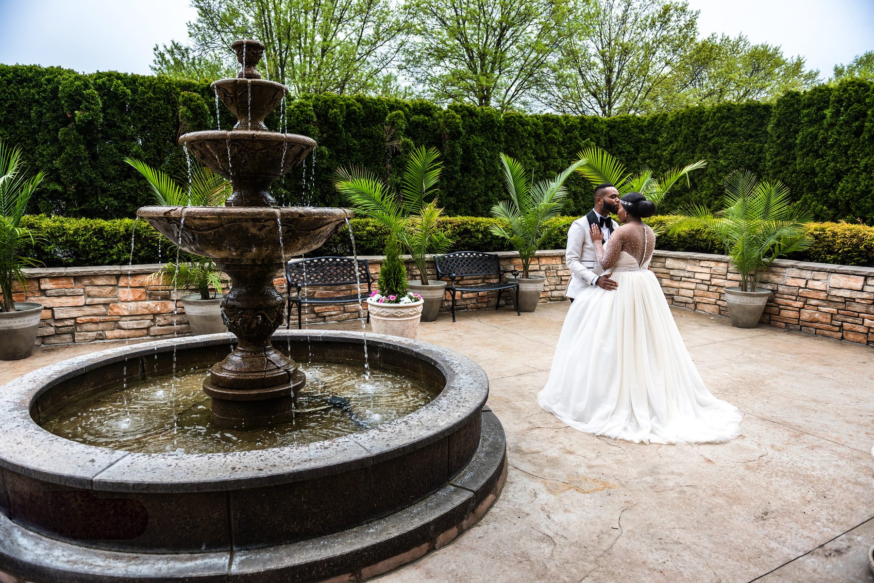 Bride and groom kissing beside a stone fountain in a garden courtyard