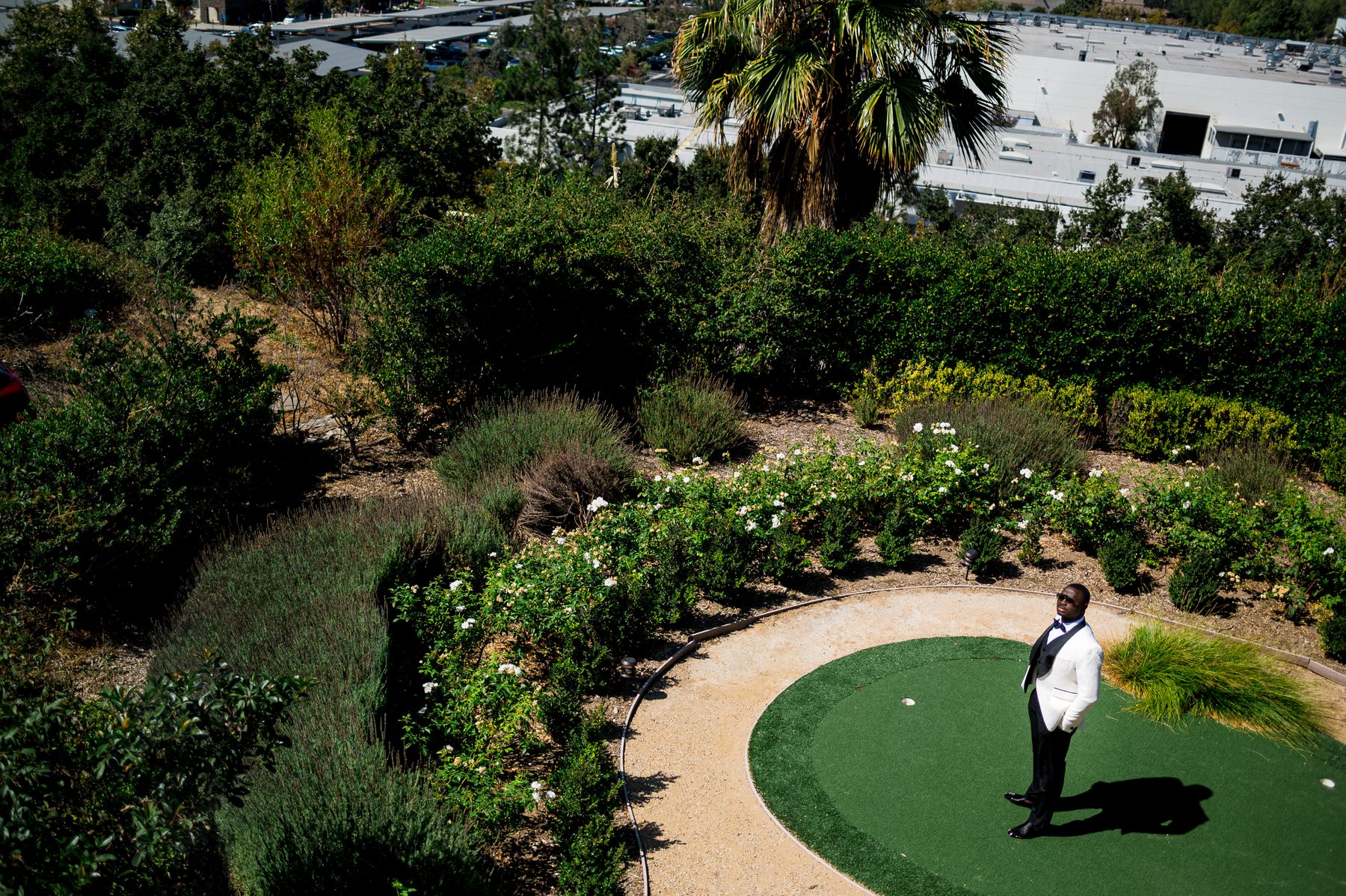 Groom in a white dinner jacket standing on a garden putting green before the ceremony