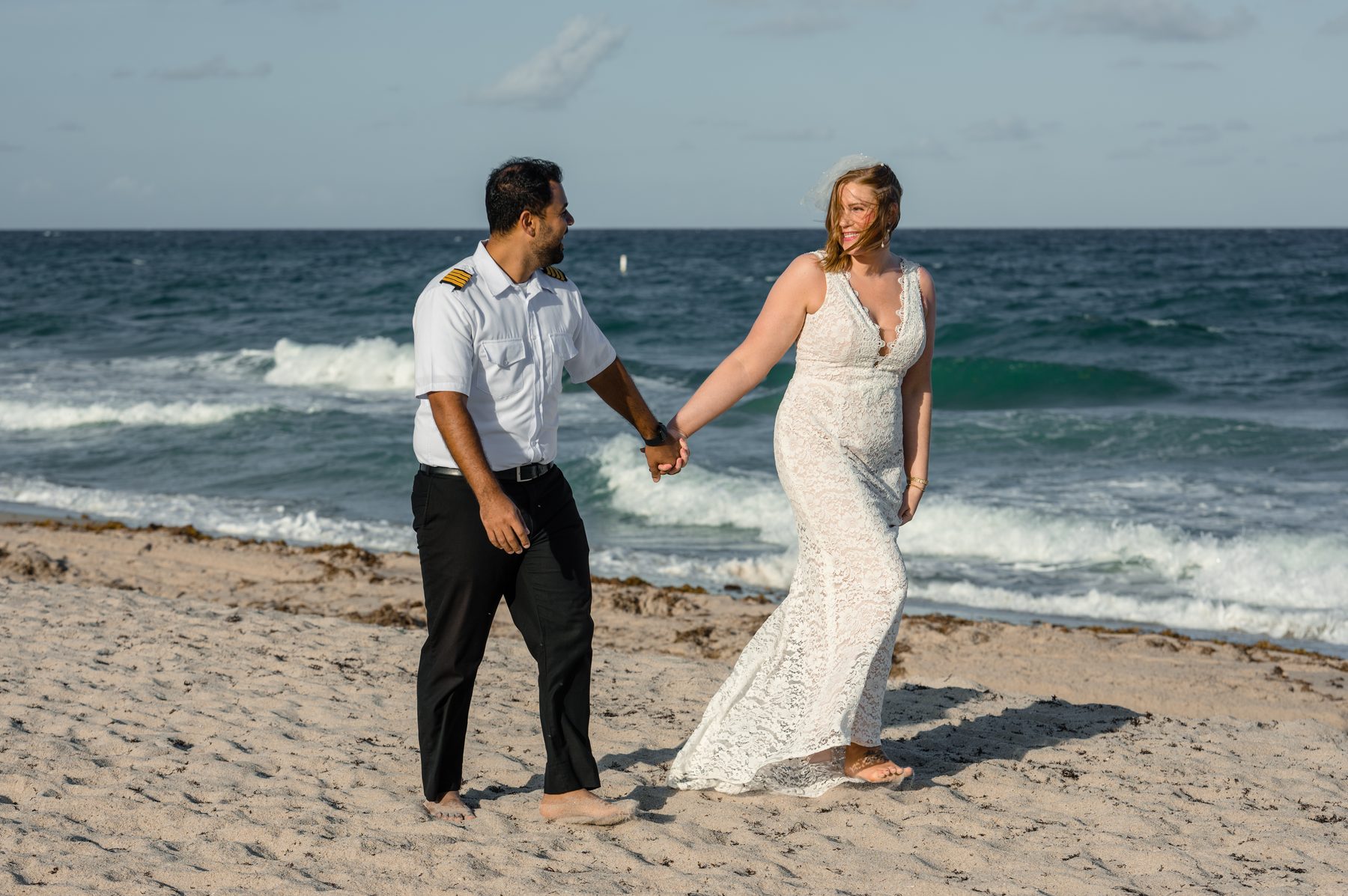 Bride and groom holding hands and walking along the beach at sunset