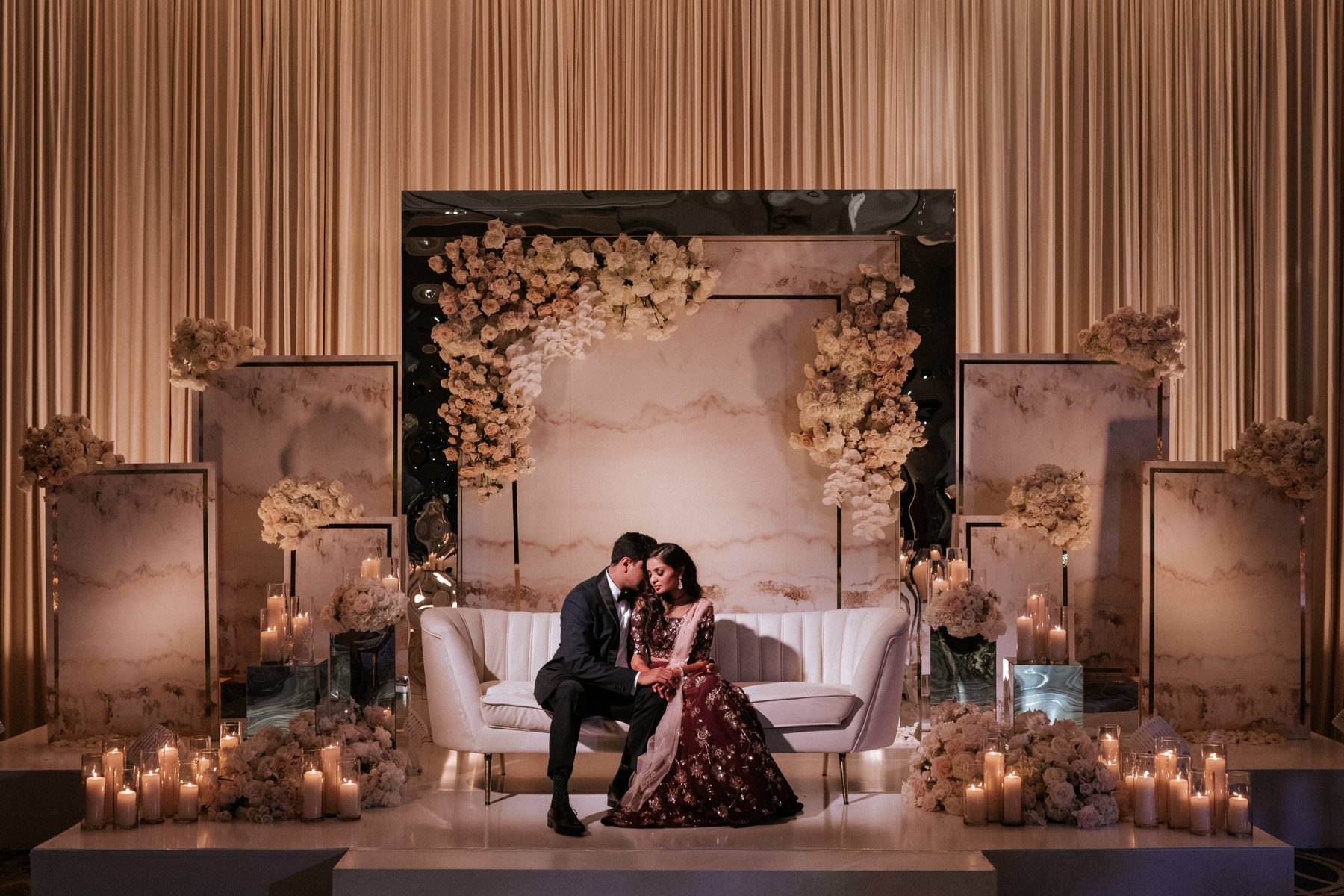 Couple seated together on a candlelit stage surrounded by floral arrangements
