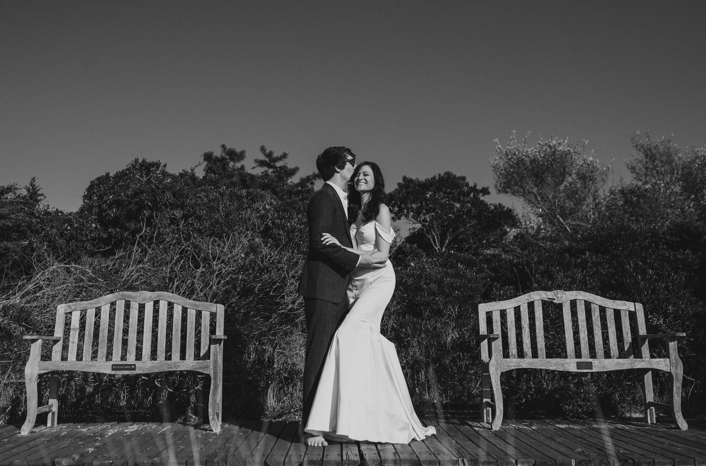 Bride and groom laughing together on a wooden deck at sunset
