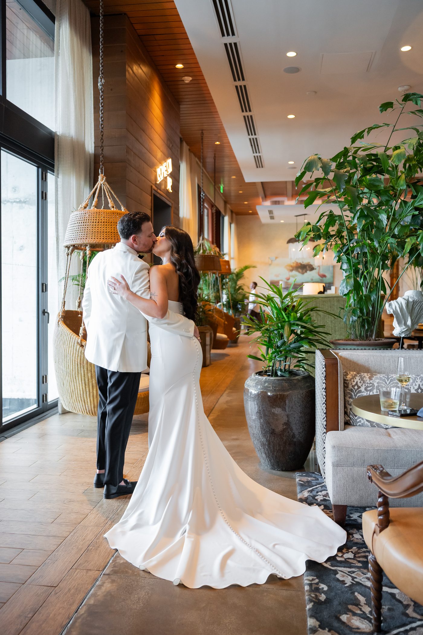 Bride and groom kissing in a plant-filled hotel lobby