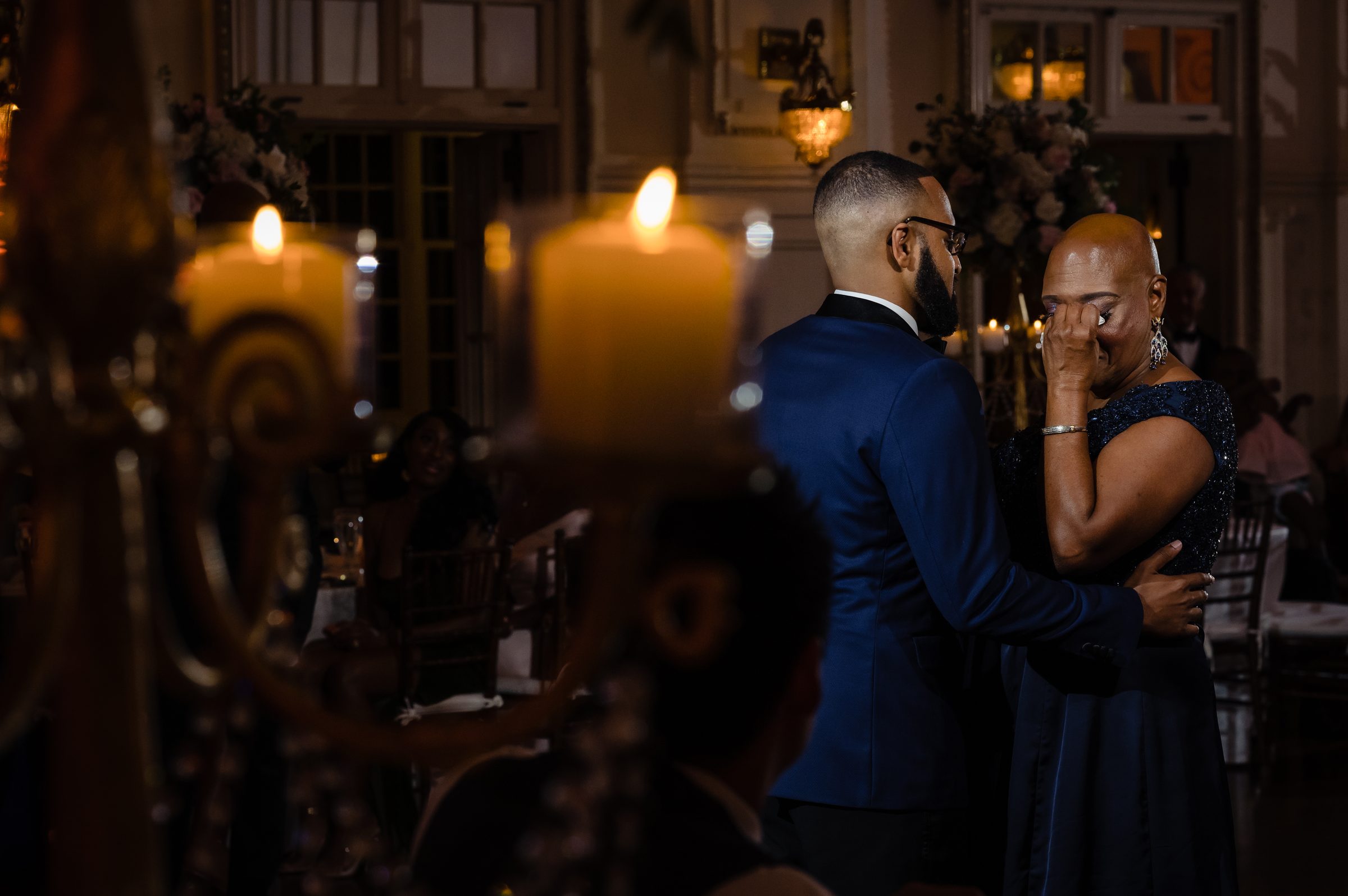 Groom comforting his emotional mother during a candlelit reception moment