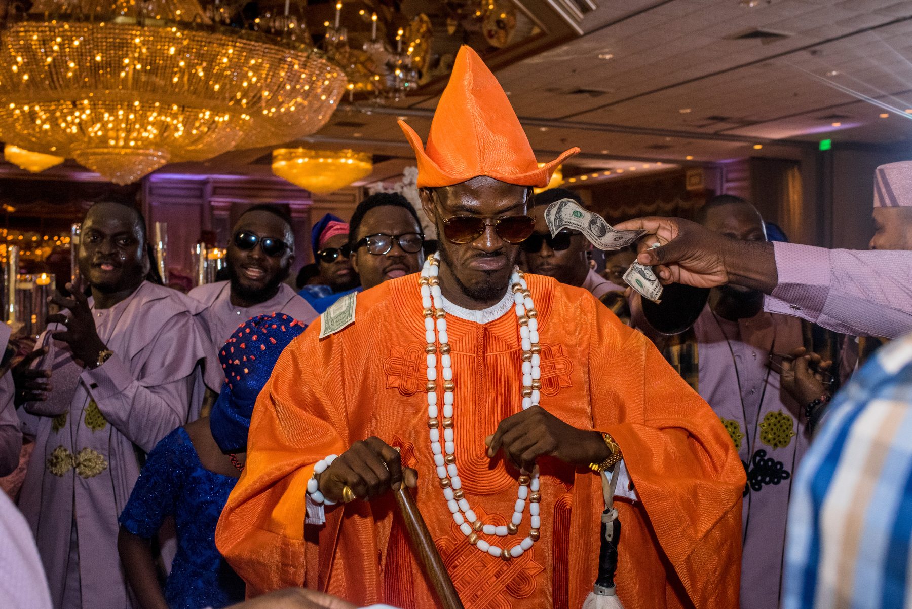 Groom in vibrant orange traditional attire and beaded necklaces at his reception