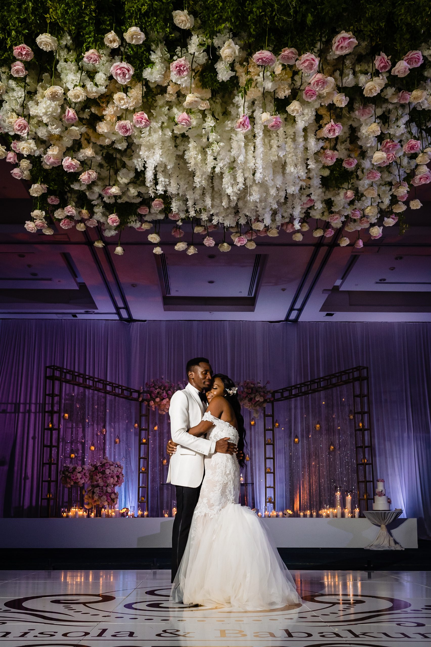 Bride and groom embracing beneath a hanging installation of white and pink roses