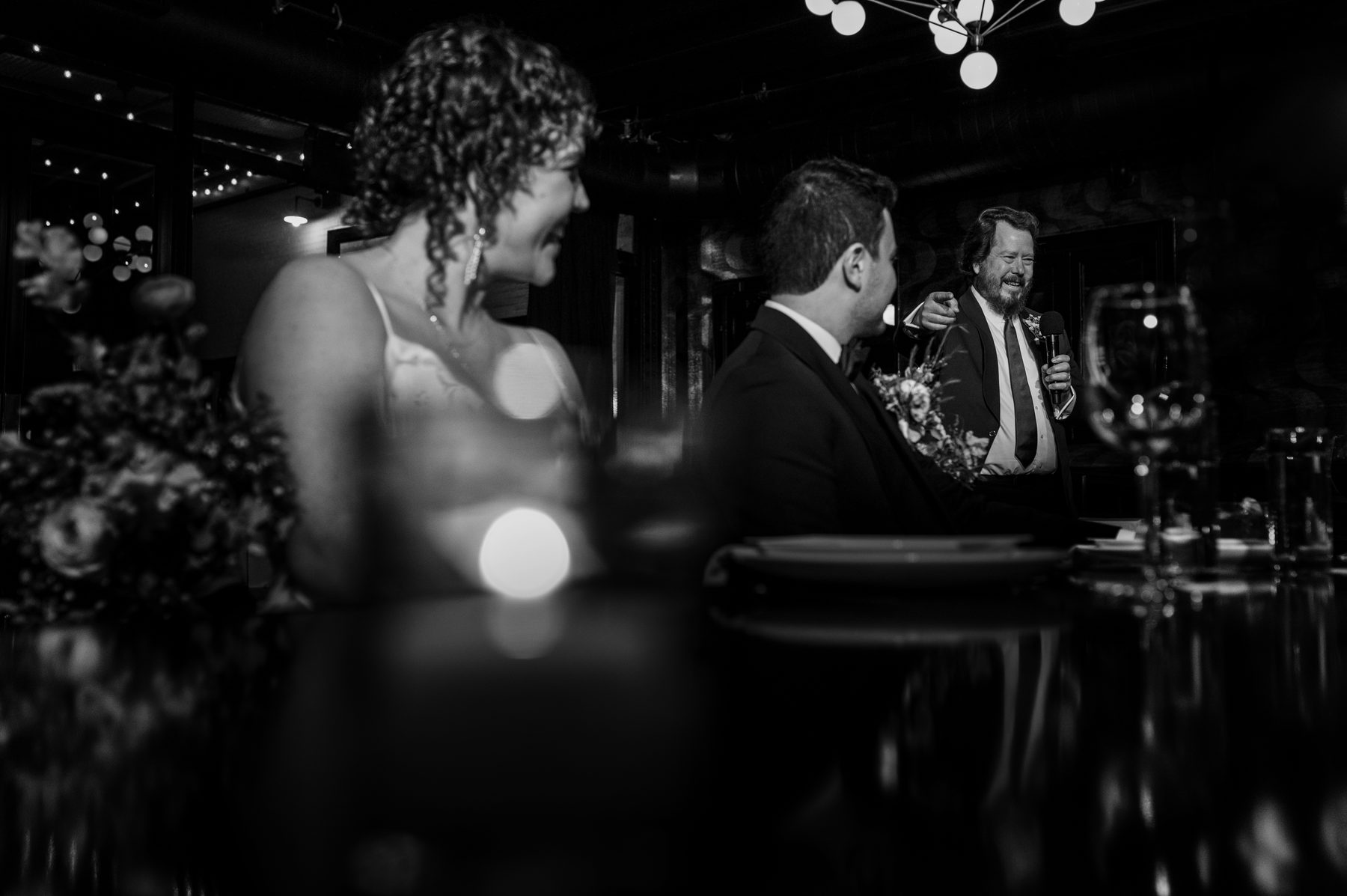 Black and white photo of a best man giving a toast beside the bride and groom
