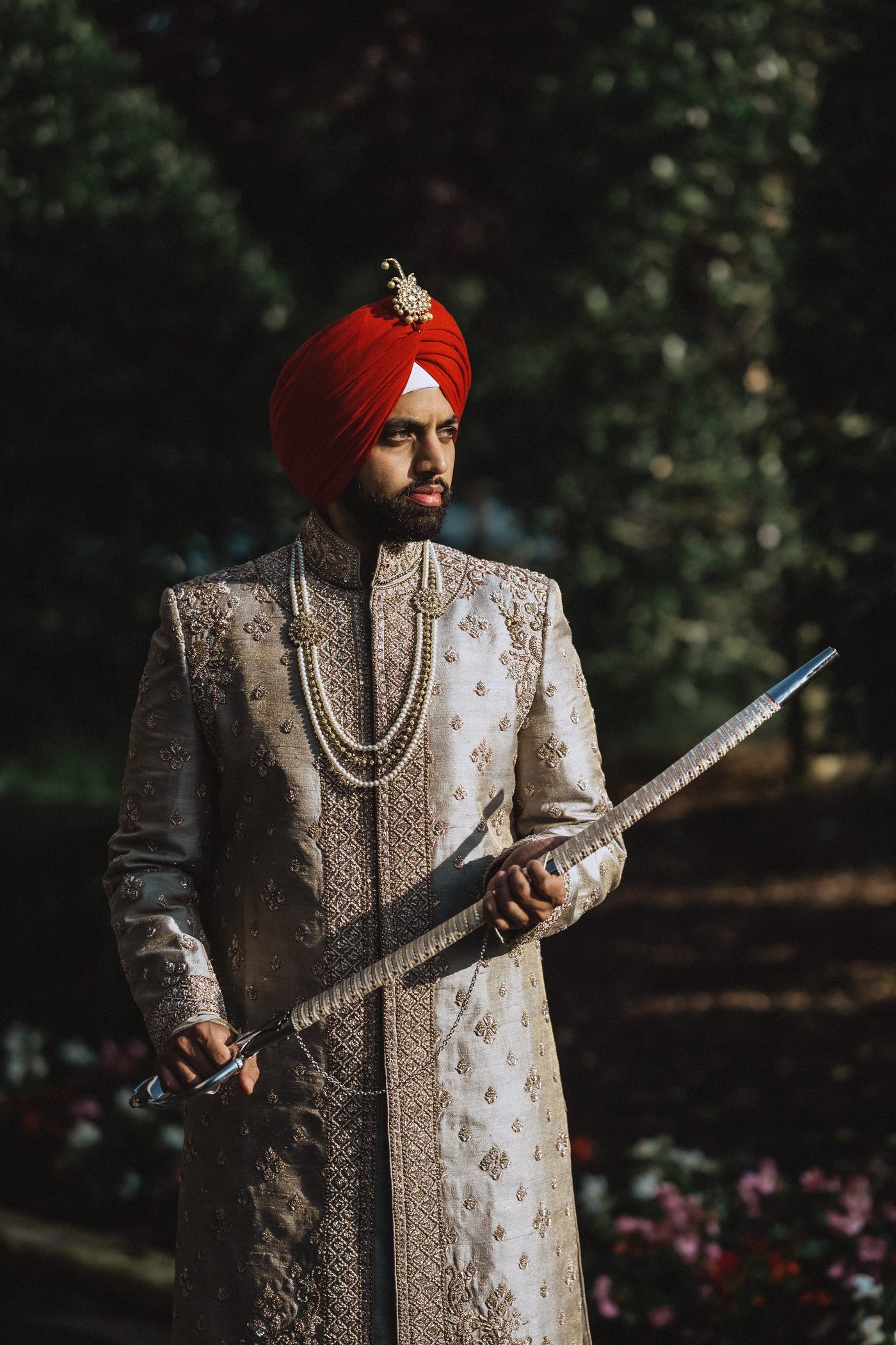 Portrait of a Sikh groom in a red turban holding a ceremonial sword