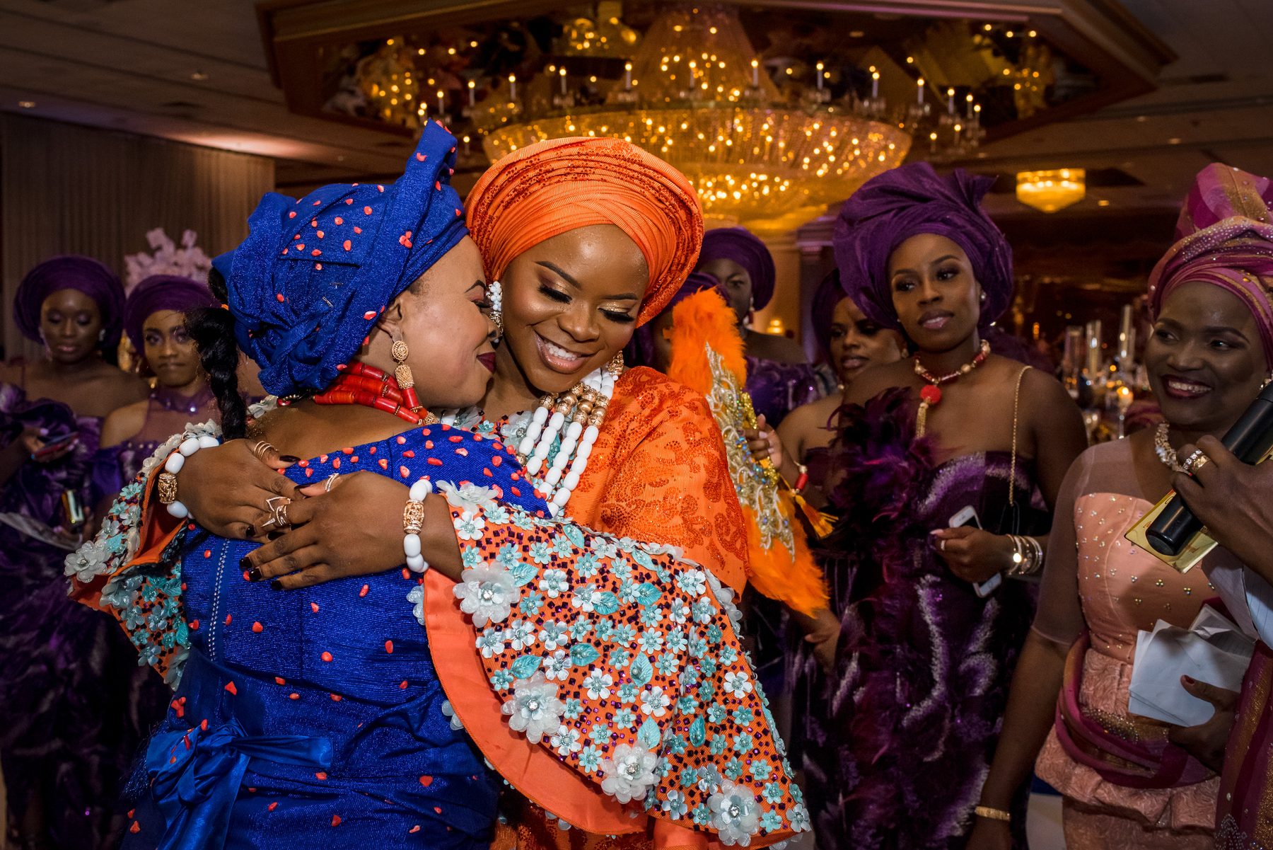 Two women in colorful traditional headwraps embracing at the reception